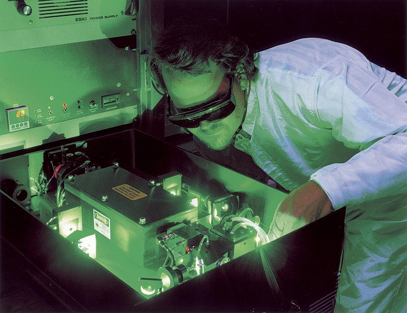 why is science important - man inspecting laser machine glowing green while wearing protective glasses